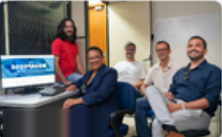 Equipe da Dosimagem sorrindo em uma sala, ao lado de um computador.